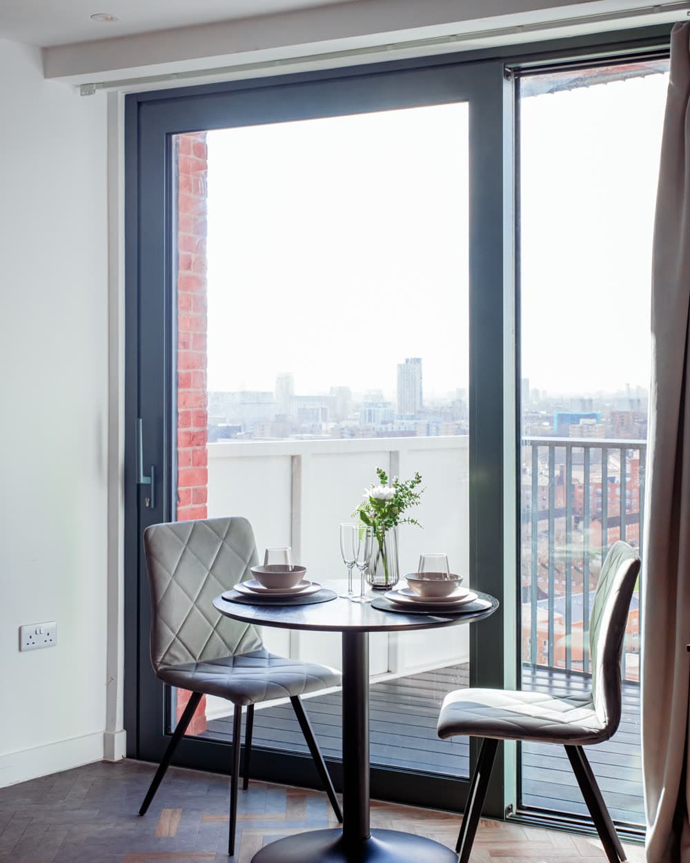 Dining table for two beside a floor-to-ceiling window in an apartment we operate